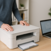 Eine Person richtet einen modernen weißen Drucker auf einem Schreibtisch im Home-Office ein. Daneben steht ein Laptop mit geöffnetem Installationsfenster