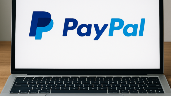 Laptop mit geöffneter PayPal-Webseite auf dem Bildschirm, daneben Smartphone mit PayPal-App auf einem Schreibtisch.