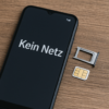 Smartphone mit geöffneter SIM-Schublade und SIM-Karte daneben auf einem Holztisch – Symbol für Mobilfunkproblem „kein Netz“